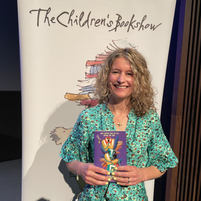 Author Ele Fountain with The Children's Bookshow banner at the Bloomsbury Theatre in London, 2023