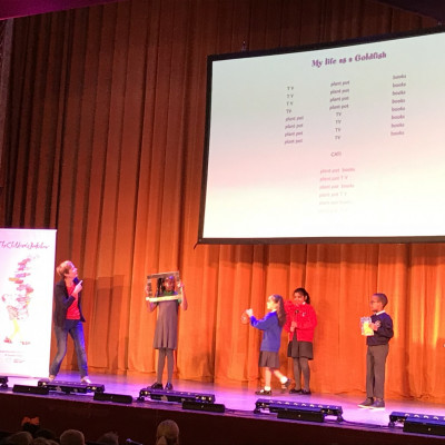 Some children come up onto stage to help Rachel perform her poem *My Life as a Goldfish*